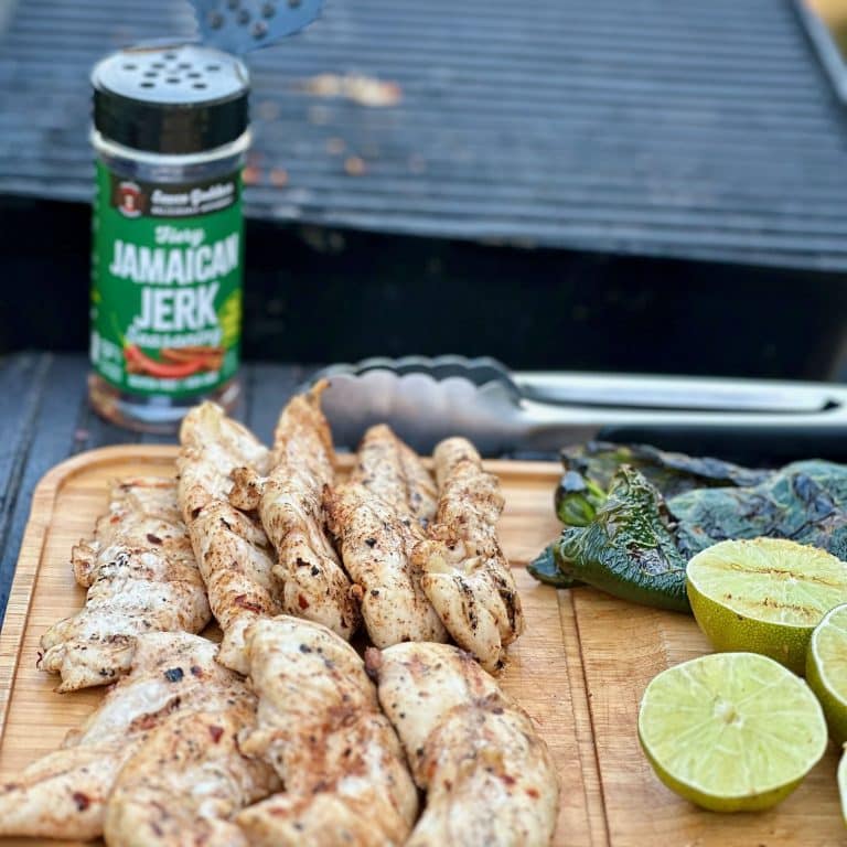 cutting board of Jamaican Jerk Chicken Tenders at the grill with the spice shaker and limes