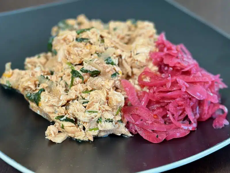 Black plater with a generous amount of Ginger Salmon Salad with a side of pickled onions, perfect for making tea sandwiches for brunch or adding to a lettuce salad